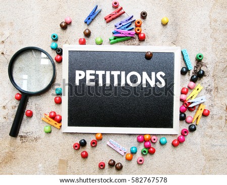 A concept image of a colorful beads and cute clothespin with a magnifying glass over a brown texture background with a chalkboard and a word PETITIONS