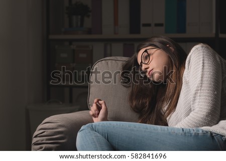 Sad young woman with glasses sitting on the couch at home, she is depressed and lonely Royalty-Free Stock Photo #582841696