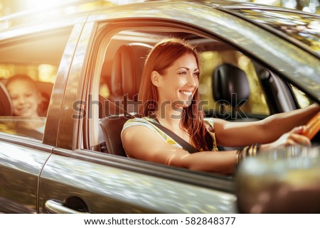 Young beautiful smiling woman driving a car.  Her cute daughter sitting on rear and enjoying. Royalty-Free Stock Photo #582848377