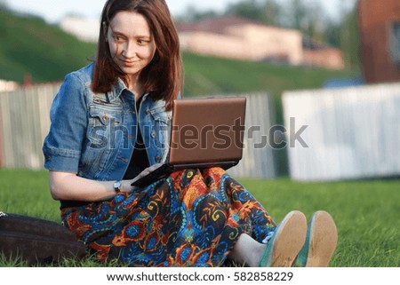 a young and pretty girl with big blue eyes handles cases in nature. Green grass and fresh air a beneficial effect on mental abilities. Beautiful female student with a laptop in the park