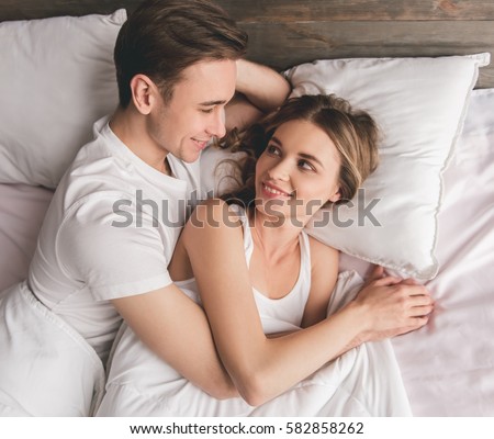 Beautiful young couple is looking at each other and smiling while lying in bed at home