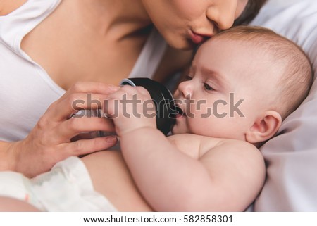Beautiful young mom is giving her cute baby drink with baby bottle and kissing her