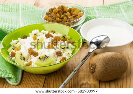 Green bowl with cottage cheese, raisins and slices of kiwi on table