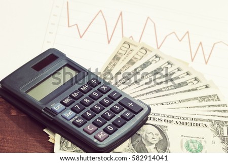 US dollars and a calculator with line chart for sales or stock market data. Business and investment concept image. Image has a vintage effect applied.
