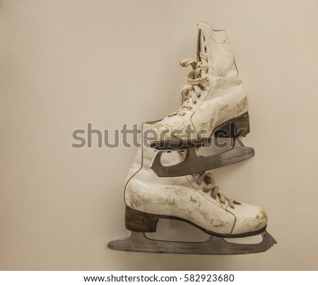 Vintage retro aged used ice skates for figure skating hanging on gray background of  beige wall. empty copy space. sport symbol, sign, idea