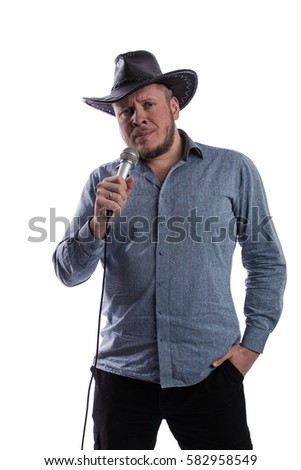 emotional actor man in a gray shirt and black hat with microphone in hands sings on a white background in studio