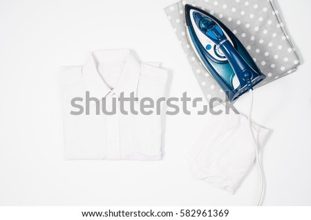 Female hand ironing clothes top view isolated on white background. Young woman with iron ironing man's shirt seen from above during housework. Blue iron on white table.