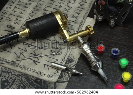 Tattoo machine with ink and sketches on tattoo skins on dark wooden background
