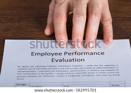 Close-up Of A Person Hand On Performance Evaluation Form At Wooden Desk