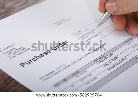 Close-up Of A Person Hand Filling A Purchase Order Form On Wooden Desk Royalty-Free Stock Photo #582995704