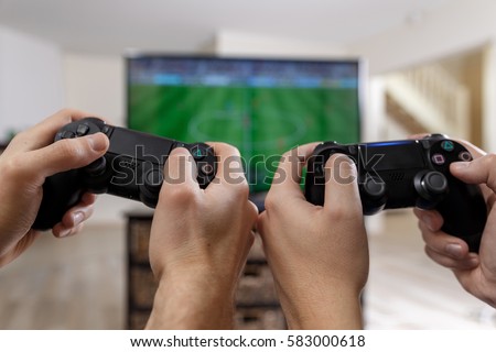 People playing video game. Hands holding console controller. Football or soccer game on the television. Widescreen tv stands on commode.