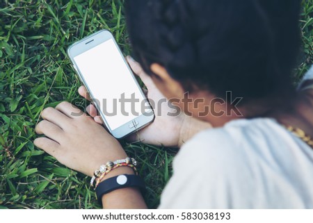 Asian teenager hold smart phone on green grass. The blank screen with copy space for your text or advertising content. Selective focus.