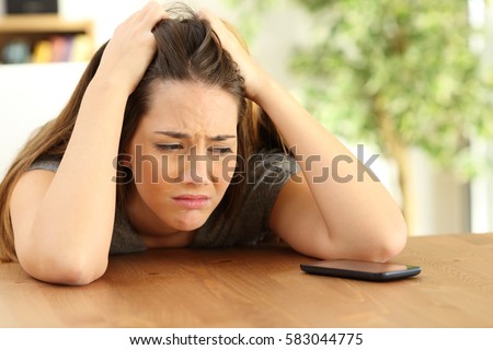 Single sad girl waiting for a phone call sitting in a table at home Royalty-Free Stock Photo #583044775