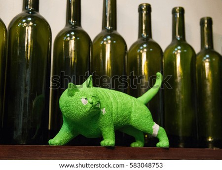 irritable green cat figurines walking on the background of row of empty green glass bottles of wine. composition, white background