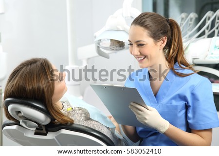 Dentist holding a medical history asking information to a patient before treatment sitting on a chair in a box Royalty-Free Stock Photo #583052410