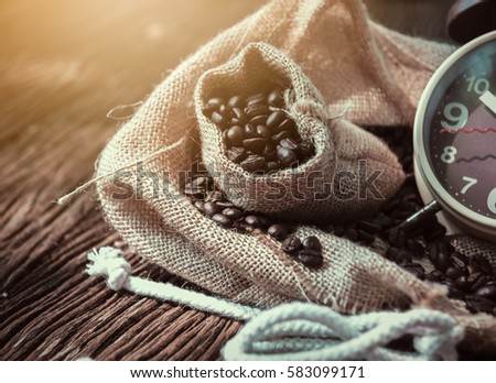 In selective focus of Vintage brouwn clock face and and coffee bean in sack fall with sunny on wooden table outdoor background.Coffee break for relax time concept- Vintage effect style pictures