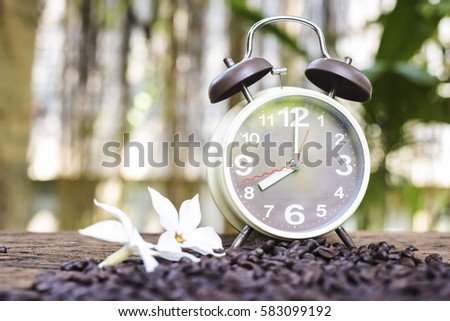 In selective focus of Vintage brouwn clock face and and coffee bean in sack fall on wooden table outdoor background.Coffee break for relax time concept- Vintage effect style pictures