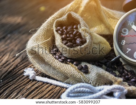 In selective focus of Vintage brouwn clock face and and coffee bean in sack fall with sunny on wooden table outdoor background.Coffee break for relax time concept- Vintage effect style pictures