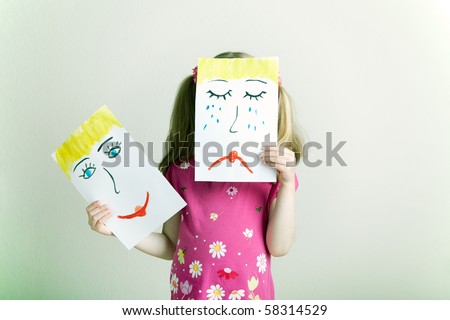 Little blonde girl holding happy and sad face masks symbolizing changing emotions
