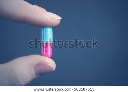 Pink and blue capsule in the human hand on a blue background