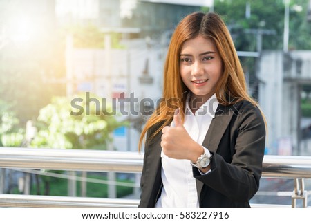 businesswoman showing thumb up gesture, city background