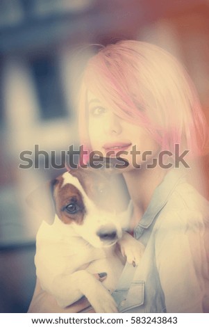 beautiful young woman standing near the window and hugging her dog
