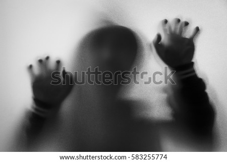 Shadow of horror man in jacket with hood.Hands on the glass.Dangerous man behind the frosted glass.Mystery man.Halloween background.Black and white picture.Blur picture