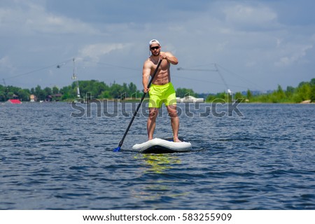 front view of athletic young man paddle boarding in sports clothing, stand up paddle