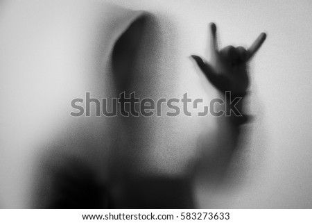 Shadow blur of horror man in jacket with hood.Hands do as a symbol love on the glass.Dangerous man behind the frosted glass.Mystery man.Halloween background.Black and white picture.Blur picture