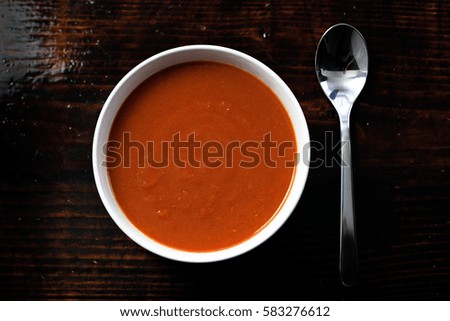 Picture of a bawl of tomato soup with a spoon on the side sitting on a wooden board