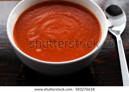 Picture of a bawl of tomato soup with a spoon on the side sitting on a wooden board