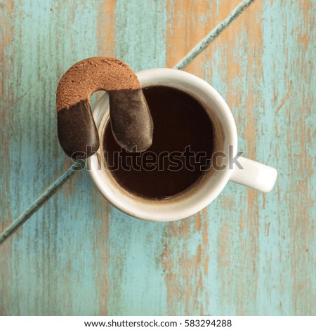 A square photo of a cookie in the form of a horseshoe on top of a white cup with black coffee, shot from above on a wooden board texture