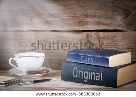Original and Copy. Stack of books on wooden desk