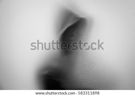 Shadow blur of horror man in jacket with hood.Dangerous man behind the frosted glass.Mystery man.Halloween background.Black and white picture.Blur picture Royalty-Free Stock Photo #583311898