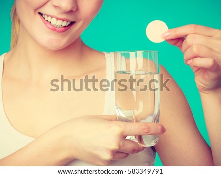 Vitamins, health, medicines. Woman holding glass with water and vitamin mineral supplement effervescent tablet. Studio shot on blue background