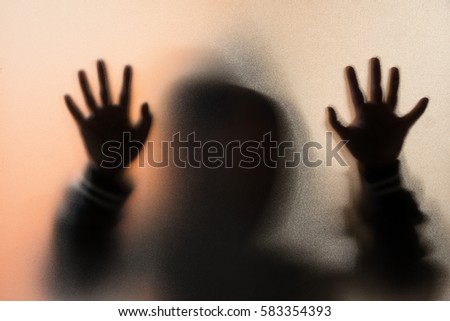Shadow blur of horror man in jacket with hood.Hands on the glass.Dangerous man behind the frosted glass.Mystery man.Halloween background.Blur picture