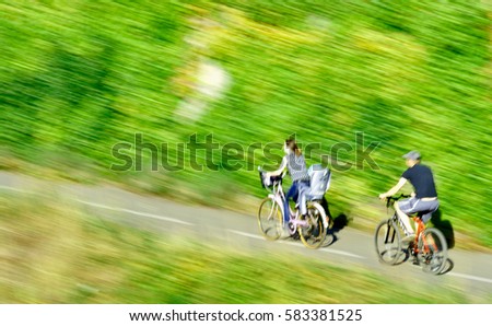 Defocused motion - Silhouettes of young family bicycling with mother carrying the little daughter children on the bike child seat and father following them on a green  green sunny park