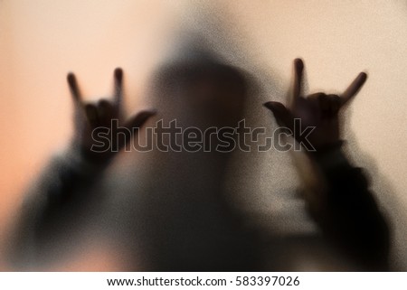 Shadow blur of horror man in jacket with hood.Finger do as a symbol love on the glass.Dangerous man behind the frosted glass.Mystery man.Halloween background.Blur picture