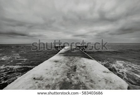 black and white photo of winter pier on the beach. heavy gray sky stern.
