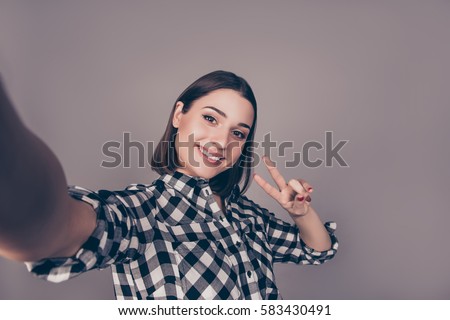 Young cheerful woman  taking a self-portrait  and gesturing v-sign against gray background