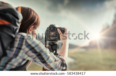 Professional hiker and photographer shooting in nature with a digital camera and a tripod, back view