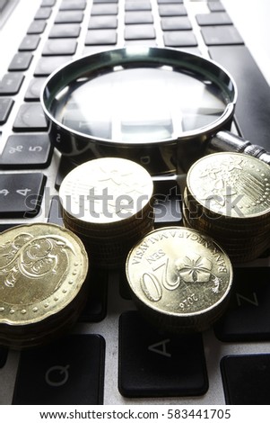 Magnify glass and coins on keyboard. Business analysis concept. Low light