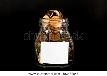 coins in a glass bottle and blank white sign on black background
