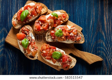 Italian bruschetta with roasted tomatoes, mozzarella cheese and herbs on a cutting board Royalty-Free Stock Photo #583515547