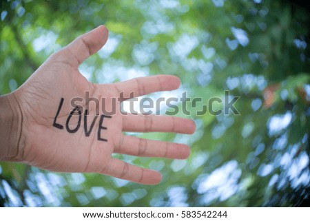 Concept Photo Of A Handwriting Word "LOVE" On The Left Hand With Blurry Heart Shape Background
