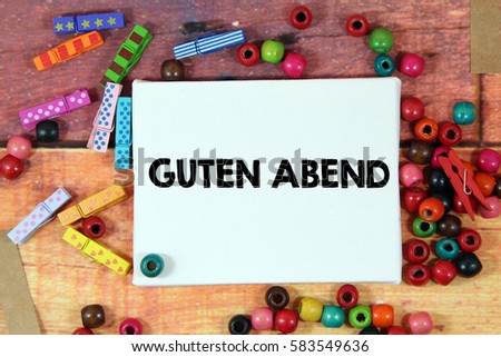 A happiness concept image of a colorful beads and cute clothespin scattered over a colorful wooden texture background with a white canvas and a word GUTEN ABEND in german mean GOOD EVENING