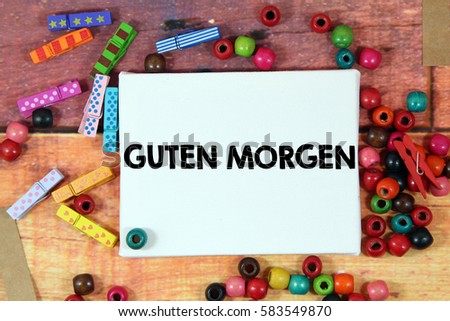 A happiness concept image of a colorful beads and cute clothespin scattered over a colorful wooden texture background with a white canvas and a word GUTEN MORGEN in german mean GOOD Evening