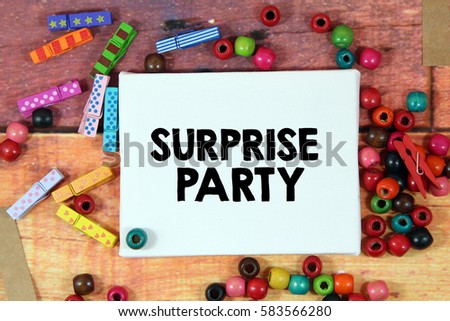 A happiness concept image of a colorful beads and cute clothespin scattered over a colorful wooden texture background with a white canvas and a word SURPRISE PARTY