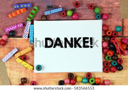 A happiness concept image of a colorful beads and cute clothespin scattered over a colorful wooden texture background with a white canvas and a word DANKE! in german mean THANK YOU