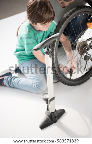 Cropped shot of father and son sitting on floor and inflating bicycle tire with pump